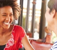 Young woman laughing, talking with friend across a café table during daytime conversation