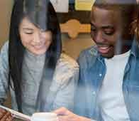 Two students smiling while looking at a phone through glass window