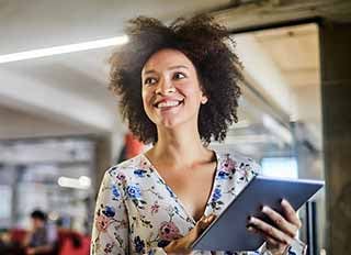Young woman holding tablet, smiling while walking through a bright coworking space