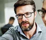 Bearded man with glasses leaning forward, discussing work with colleague