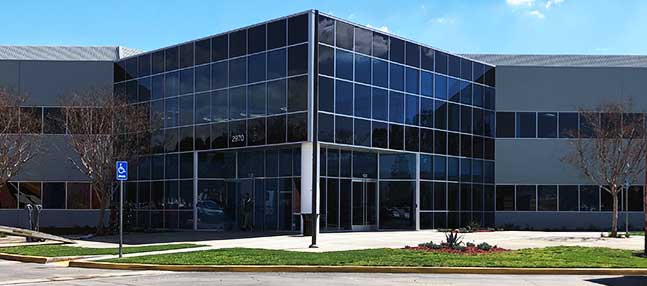 Glass-fronted office building entrance with landscaped lawn and parking