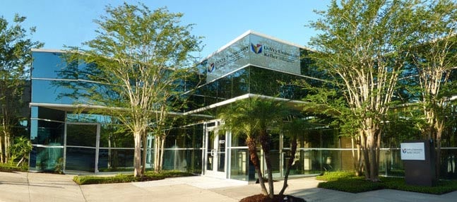 Modern glass office building entrance framed by trees and palms