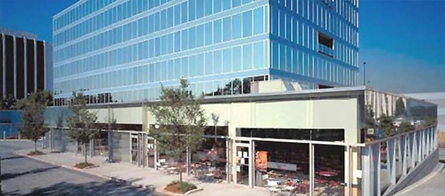 Ground-floor retail storefronts beneath glass office tower along tree-lined sidewalk