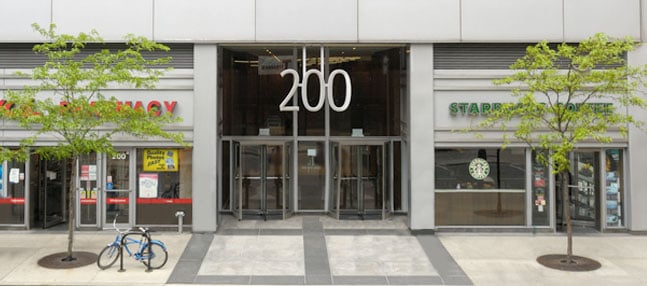Revolving entrance doors beneath "200" with storefronts and parked bicycle