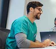 Healthcare professional taking notes during team meeting with laptop