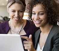 Two professional women smiling and pointing at laptop screen during meeting