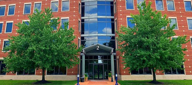 Two trees framing office building glass entrance with "2" above door