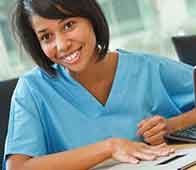Smiling healthcare worker in blue scrubs reviewing patient paperwork at desk
