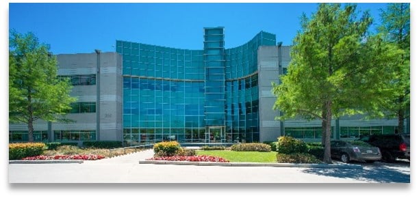 Modern blue-glass office building with landscaped entrance and parked cars