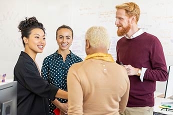 Colleagues greeting and shaking hands in bright office meeting space during morning team meeting