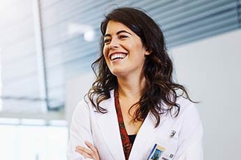 Smiling female doctor with arms crossed in bright clinical office