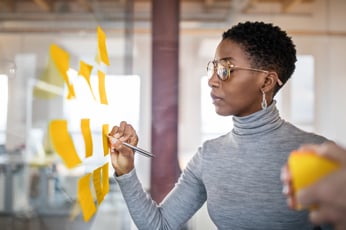Person writing on yellow sticky notes on glass wall during brainstorming session