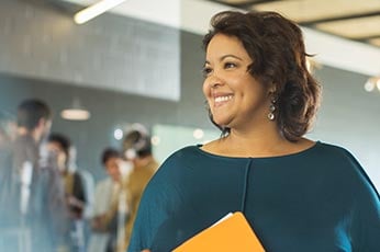 Smiling professional woman holding orange folder in a bright open-plan office