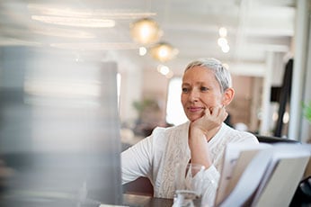 Older woman thoughtfully reviewing computer screen in bright modern office