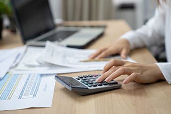 Hands using calculator to compute figures with financial documents and laptop on desk