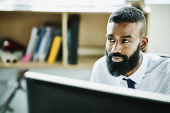 Bearded man concentrating while working at computer in modern office environment