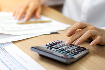 Person pressing calculator keys while reviewing financial documents on desk