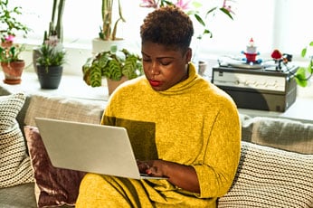 Person focused on laptop typing on couch surrounded by houseplants