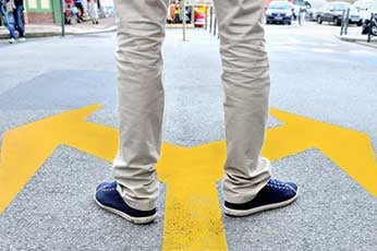 Person's legs standing on street at yellow forked arrows indicating left and right choices