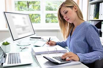 Woman calculating expenses and writing in a binder at desk