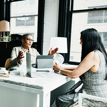 Two colleagues discussing a project across a bright office desk with laptop