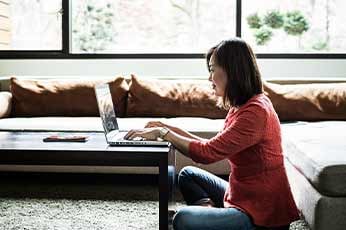 Person typing on laptop while sitting on living room floor near sofa
