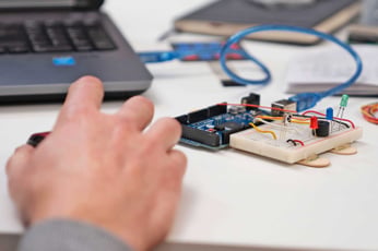 Person's hand adjusting Arduino microcontroller and breadboard circuit next to laptop