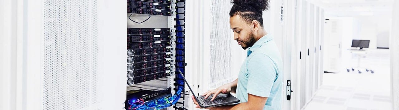 IT technician diagnosing rack servers using laptop in bright data center
