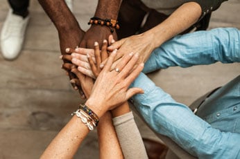 Five diverse team members stacking their hands to represent business team unity.