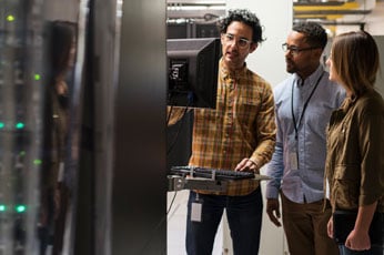 Three diverse technicians using a comuter in a server room.