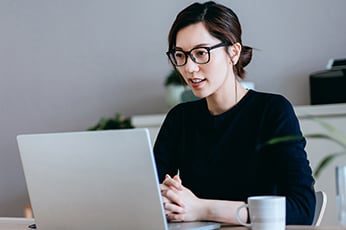 Woman in glasses participating in video call at home office with coffee mug