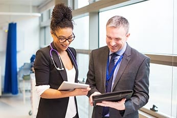 Two medical professionals reviewing tablets together in hospital corridor