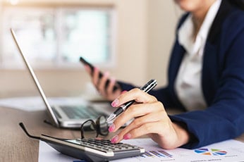 Business person using calculator and smartphone beside laptop, reviewing financial charts