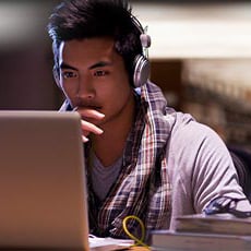 College student wearing headphones studying intently at laptop in library late night