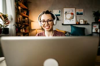 Woman wearing headphones smiling while video-chatting from cozy home office