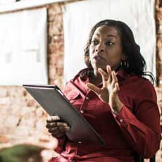 Middle-aged woman holding a tablet, gesturing emphatically while leading a discussion