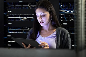 IT technician checking tablet while monitoring network servers in server racks