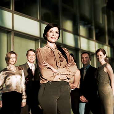 Confident businesswoman arms crossed standing with colleagues in modern office lobby