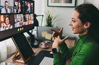 Woman in green sweater signing during remote group video conference at home desk