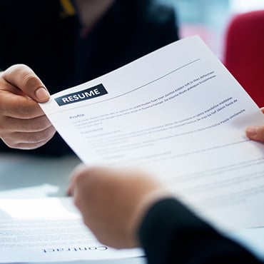Person handing a paper with "RESUME" header across desk during interview