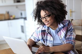 Young woman with glasses typing on laptop at bright kitchen table