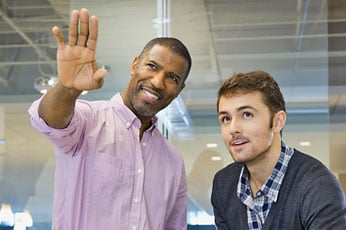 Senior colleague pointing while teammate listens in glass-walled office