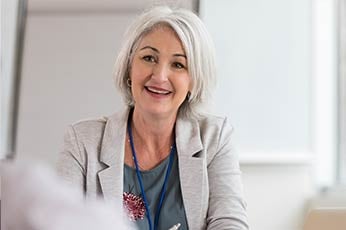Professional woman smiling warmly while participating in a small office meeting.
