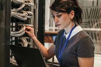 Technician inspecting network cables while configuring servers with laptop in rack room