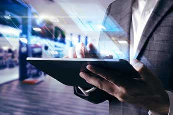 Businessperson tapping tablet displaying translucent digital interface in modern transit hub
