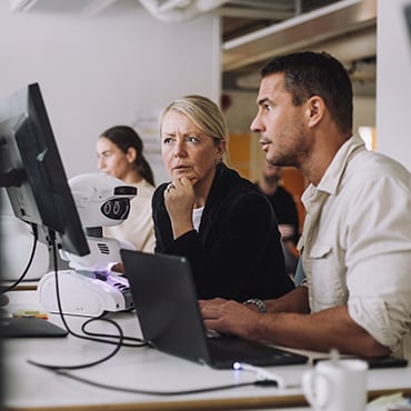 Woman and man reviewing project on laptop and monitor in modern open office