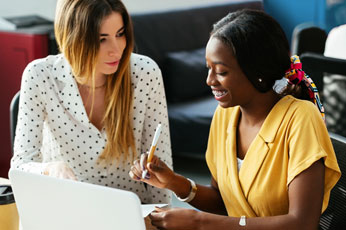 Two smiling colleagues pointing at a document by laptop, discussing project