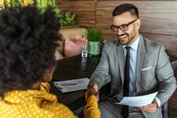 Smiling businessman in gray suit shakes hands with candidate across wooden office table