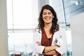 Smiling female doctor standing with arms crossed in medical office