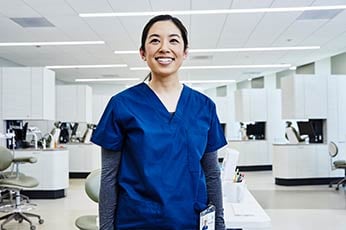 Smiling healthcare worker in blue scrubs standing in bright dental clinic operatory